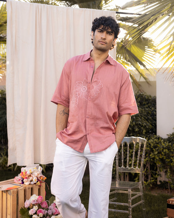 Man wearing a pink shirt with a floral design and white pants standing outdoors.
