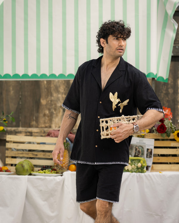 Man in black outfit with decorative elements standing outdoors under a striped awning.