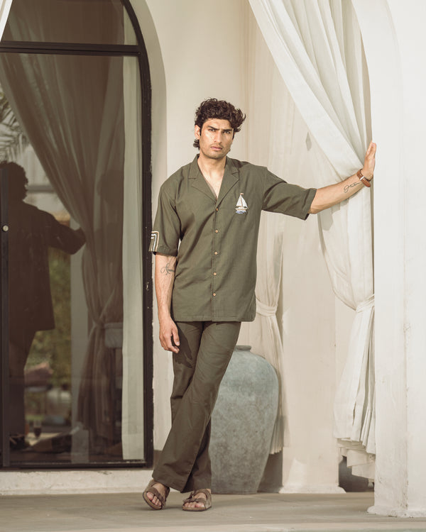 Man in a green shirt and pants standing in a room with white curtains.