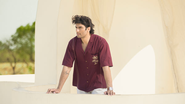 Man wearing a maroon shirt with a logo, standing in front of a beige tent outdoors.