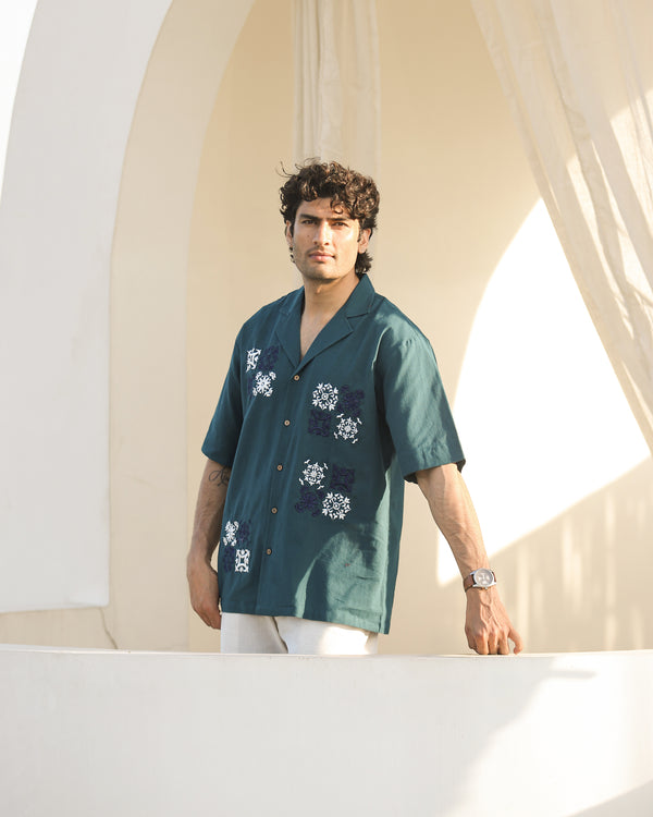 Man wearing a teal shirt with floral patterns standing in front of a white archway.