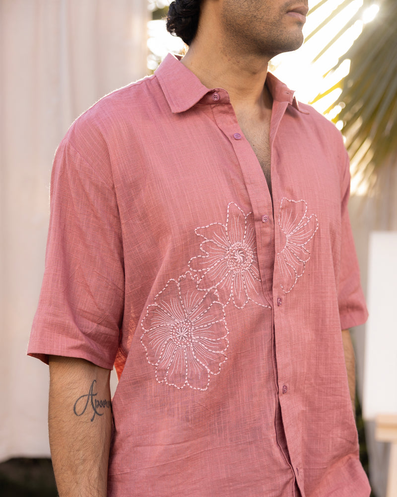 Man wearing a pink shirt with floral embroidery in an outdoor setting