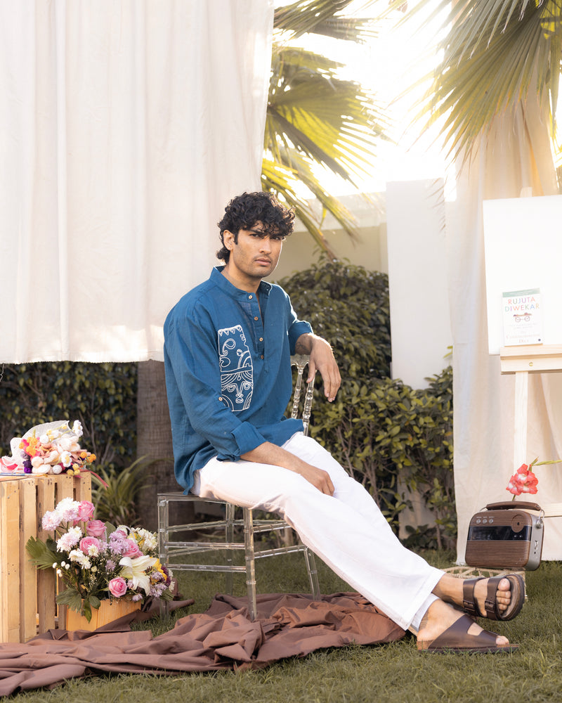 Man sitting on a chair outdoors with plants and flowers in the background