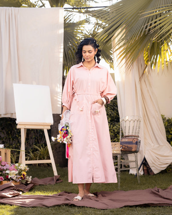 Woman in a pink dress standing outdoors with greenery and draped fabric in the background