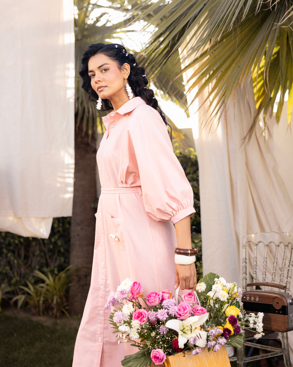 Woman in a pink dress holding flowers outdoors with palm leaves in the background