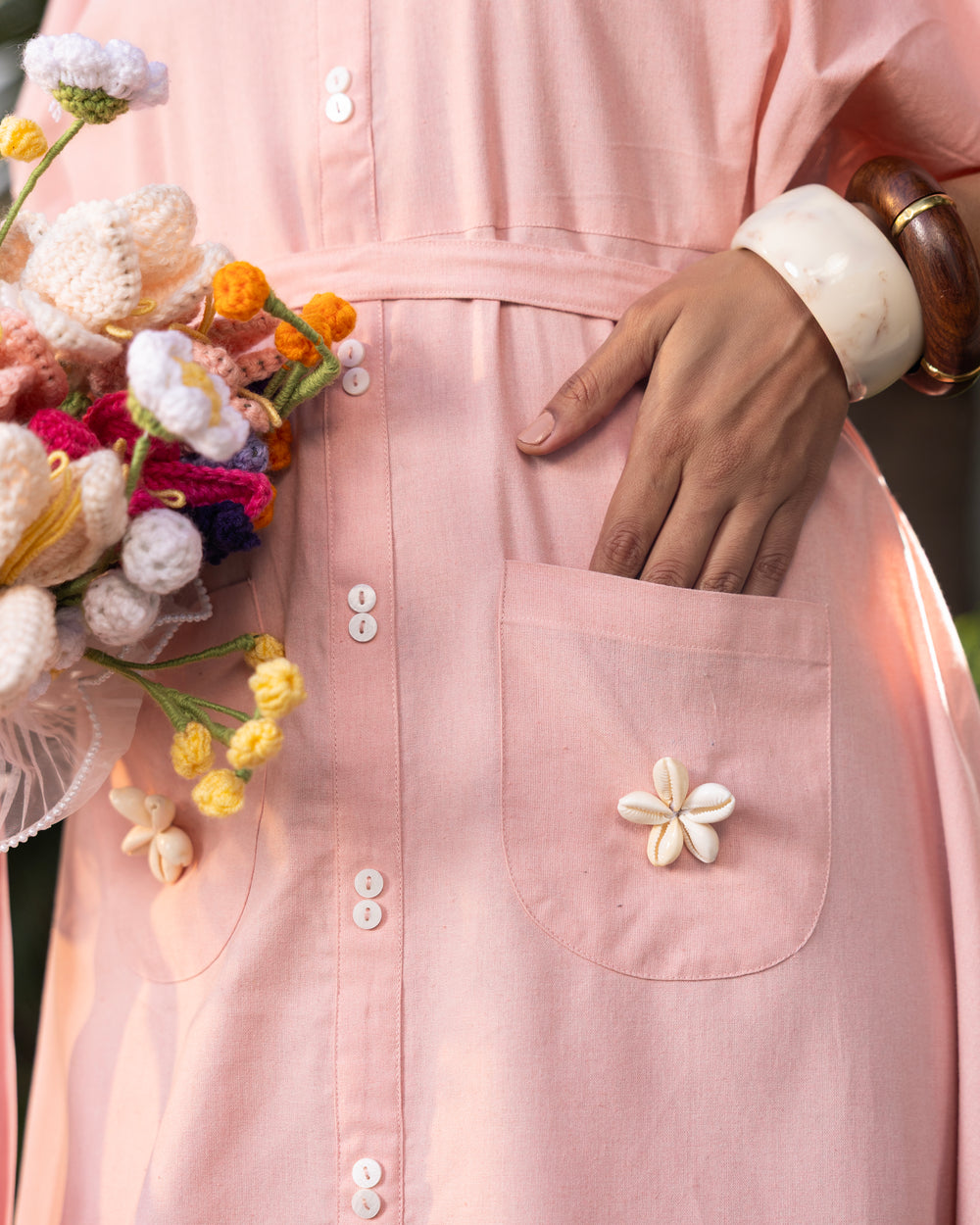 Person wearing a pink dress with floral embellishments holding a bouquet of flowers.