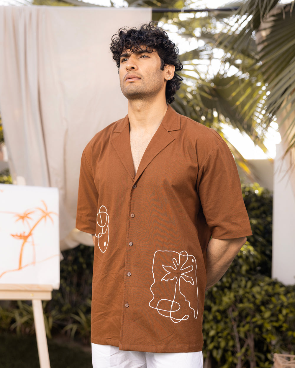 Man wearing a brown shirt with white designs outdoors