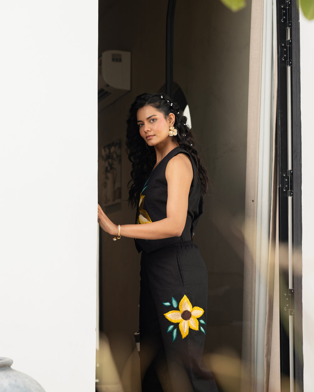 Woman wearing black cotton flex embroidered co ord set with floral waistcoat and straight pants near doorway