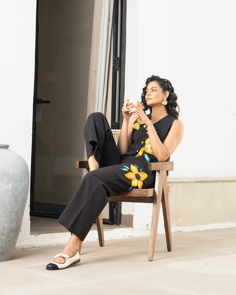 Woman sitting in black cotton flex embroidered co ord set with floral waistcoat top and straight pants