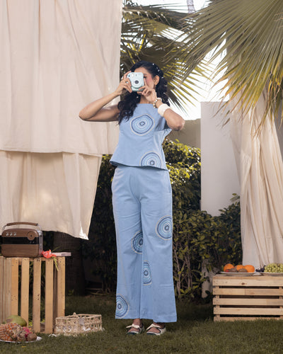 Woman taking a mirror selfie outdoors with a light blue outfit featuring circular patterns.