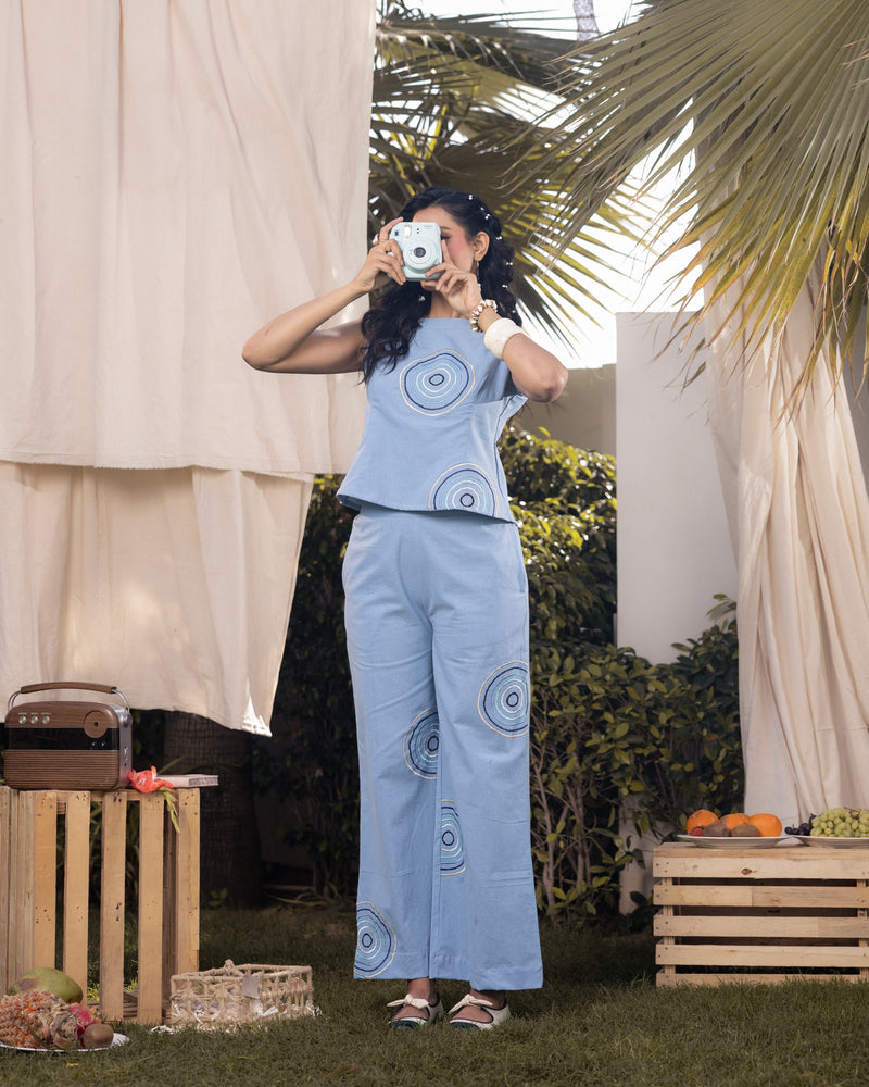 Woman taking a mirror selfie outdoors with a light blue outfit featuring circular patterns.