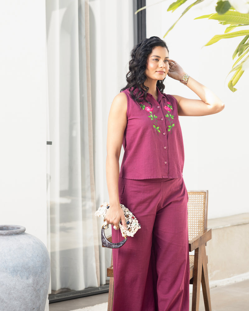 Woman in a purple outfit with floral embroidery standing indoors.