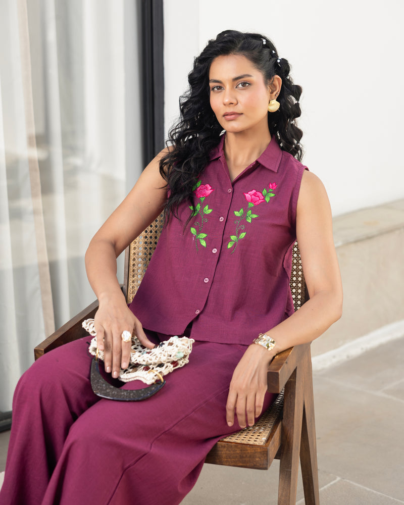 Woman wearing a purple outfit with floral embroidery, sitting indoors.