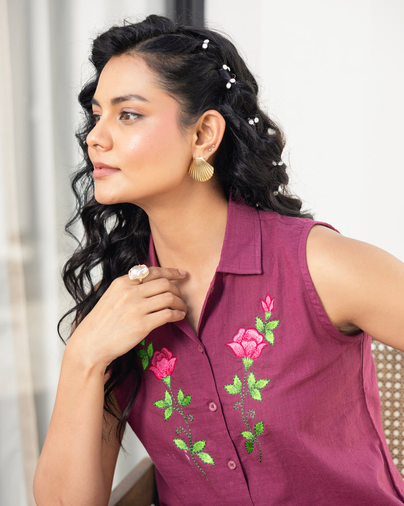 Woman wearing a maroon sleeveless top with floral embroidery against a neutral background
