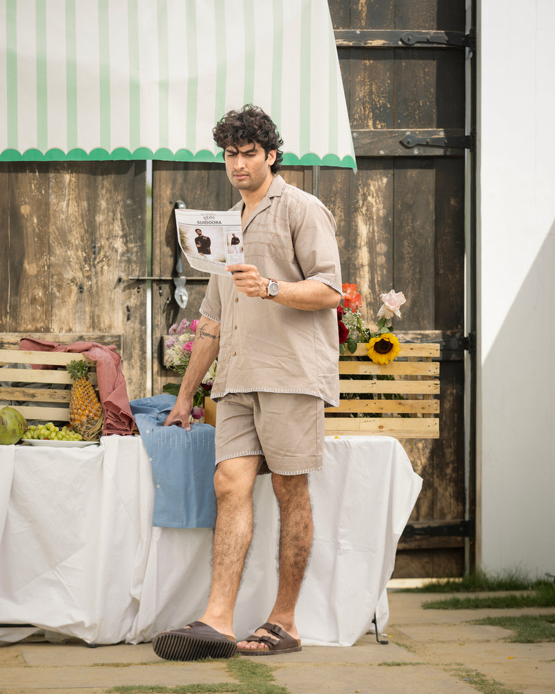 Man reading a newspaper outdoors with a rustic wooden building in the background