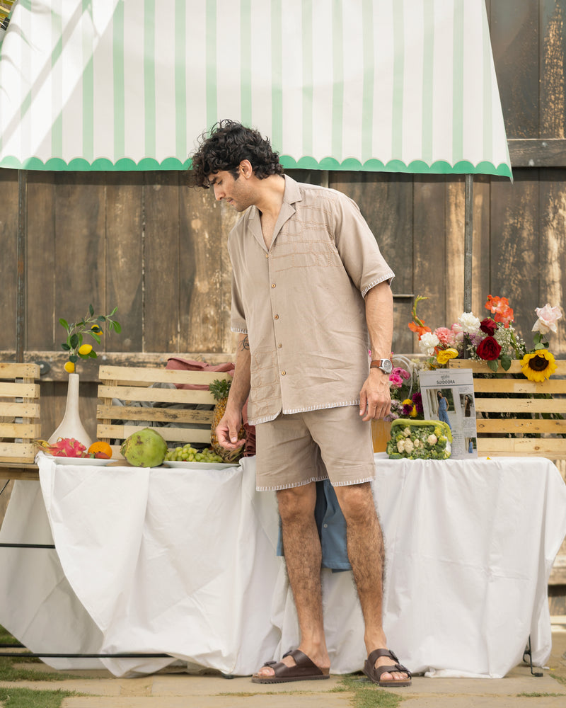 Man standing outdoors by a table with fruits and flowers, under a green and white striped canopy.
