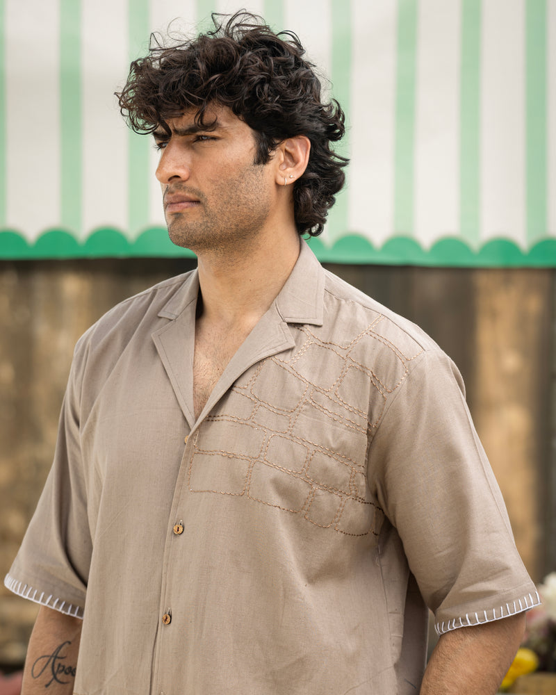 Man wearing a beige shirt with a green and white striped awning in the background
