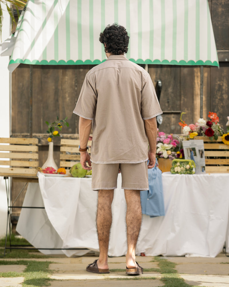 Man in beige shirt and shorts standing in front of a decorated outdoor table with flowers and a striped canopy.