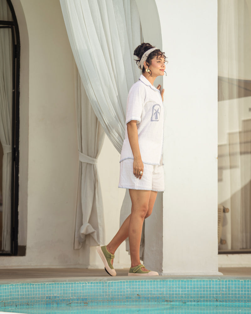 Woman in a white outfit standing by a poolside with curtains in the background