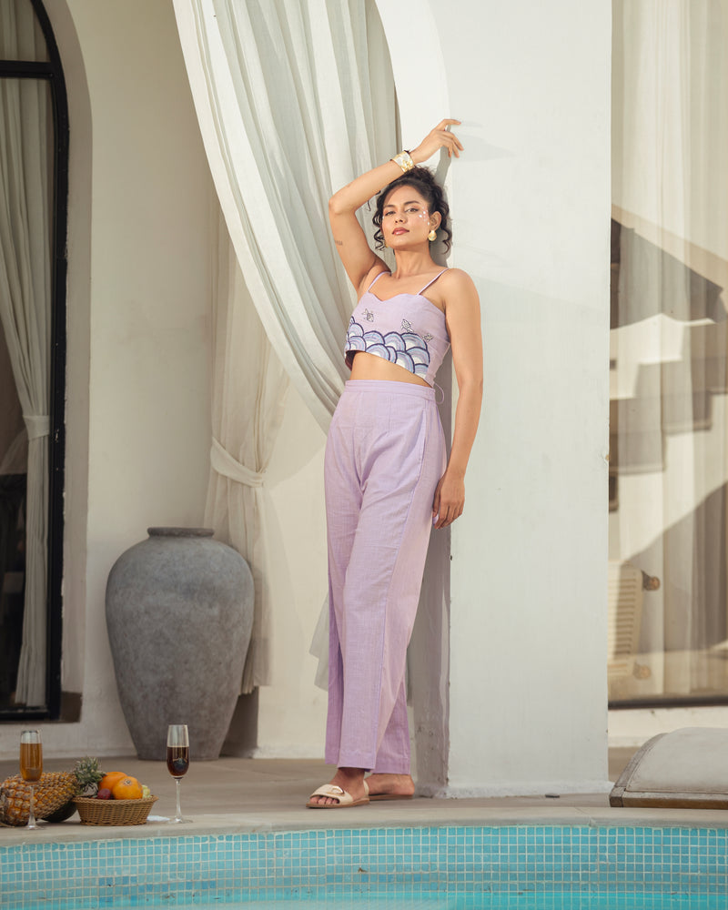 Woman in a lavender outfit standing by a poolside with curtains in the background