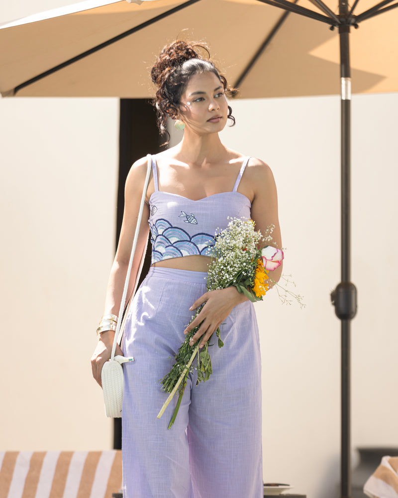 Woman in a light purple outfit holding flowers under an umbrella