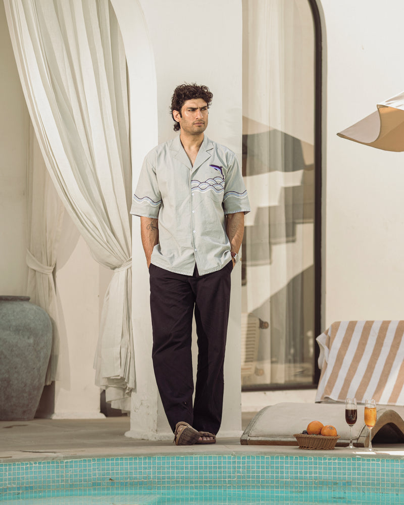 Man standing by a poolside wearing light-colored pajama top and dark pants.