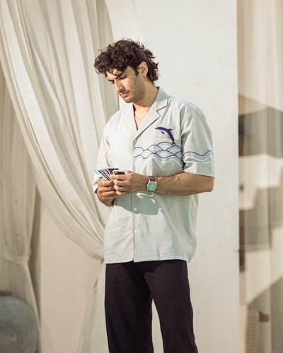 Man wearing a white shirt with a design, holding cards, standing in front of a white curtain.
