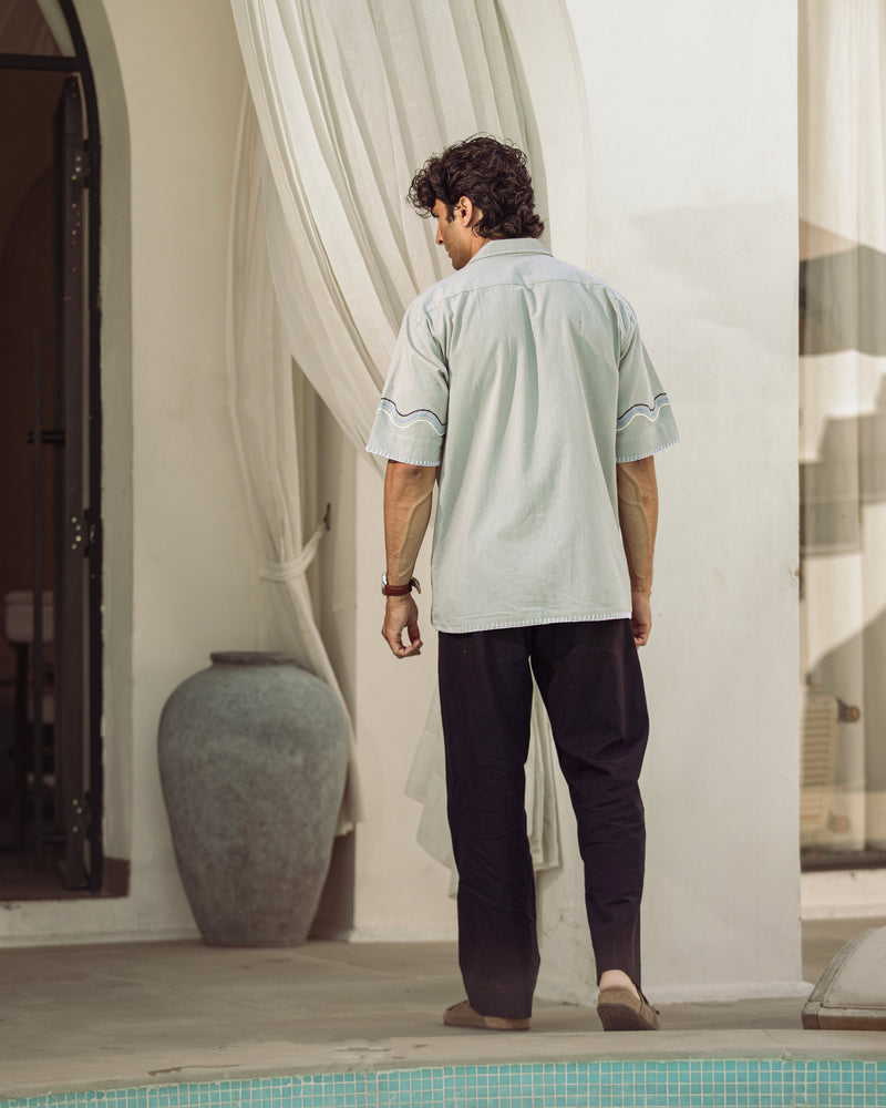 Man standing by a poolside with a white curtain and decorative vase in the background