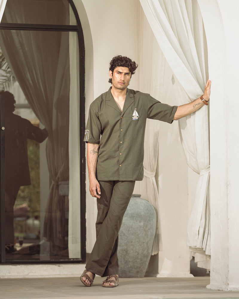 Man in a green shirt and pants standing in a room with white curtains.