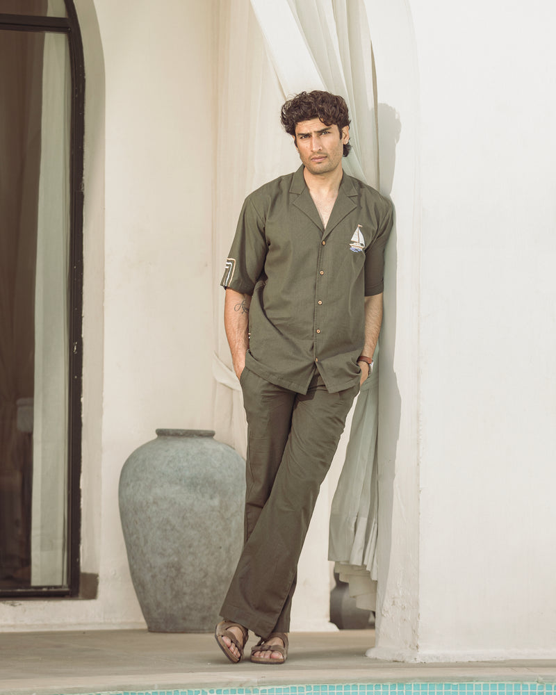 Man wearing a green shirt and brown pants standing by a poolside.