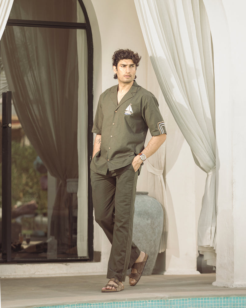 Man in green outfit standing by a poolside with white curtains in the background