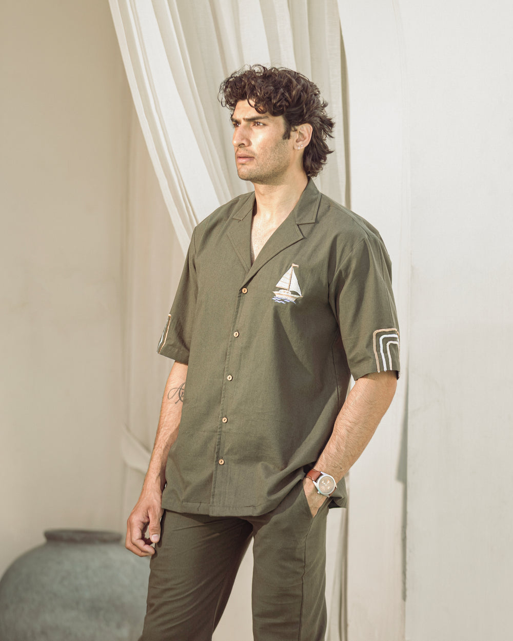 Man wearing a green shirt with a logo, standing against a neutral background