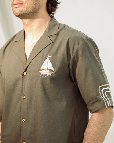 Man wearing a green shirt with a sailboat emblem on a plain background