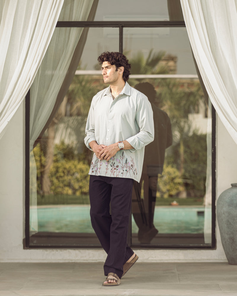 Man standing in a modern indoor setting with large windows and white curtains.

