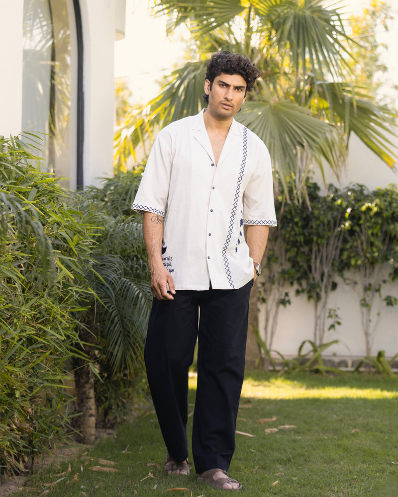 Man wearing a white shirt with black pants standing in a garden.
