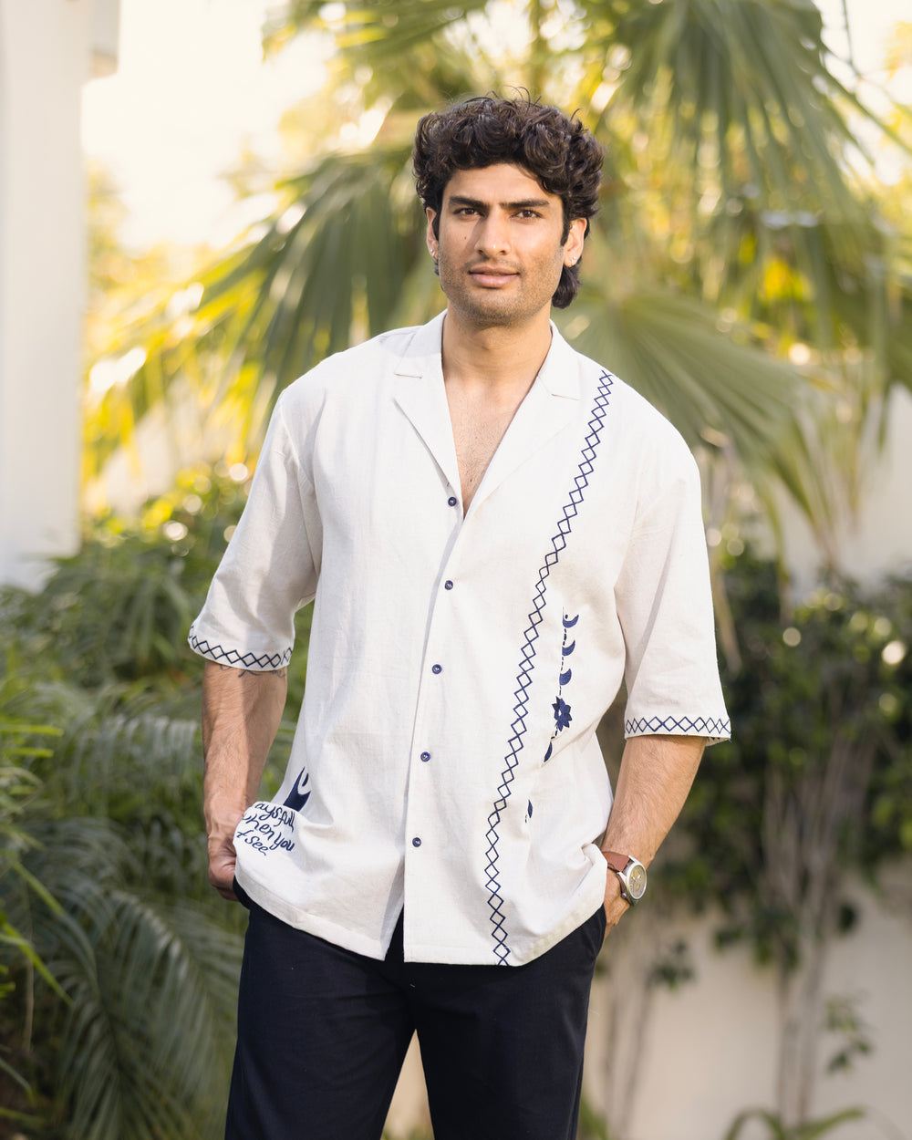 Man wearing a white embroidered shirt with a blurred green outdoor background