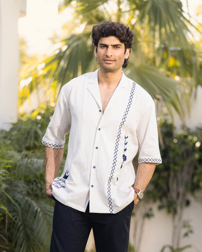 Man wearing a white embroidered shirt with a blurred green outdoor background