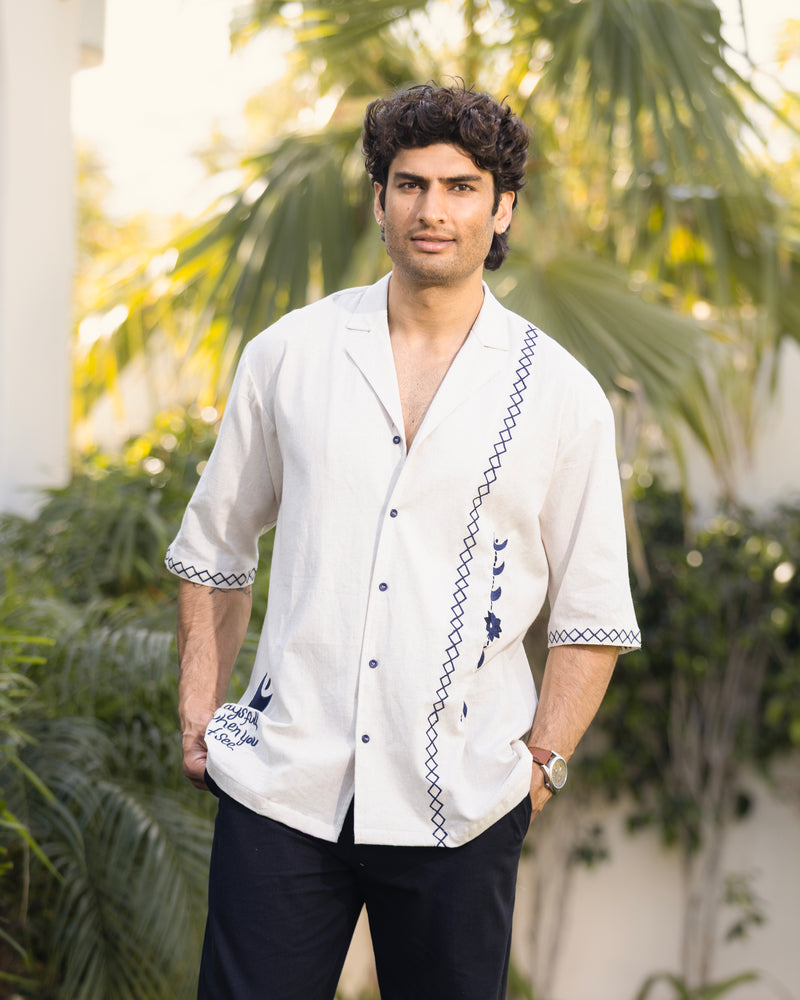 Man wearing a white embroidered shirt with a blurred green outdoor background