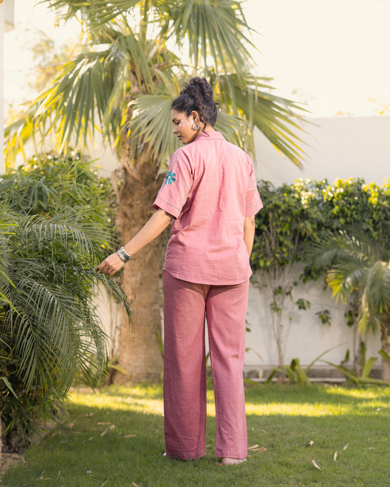 Person wearing a pink outfit standing in a garden with palm trees.