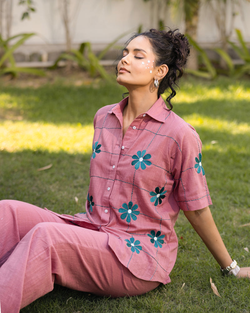 Woman in a pink outfit with floral patterns sitting on grass