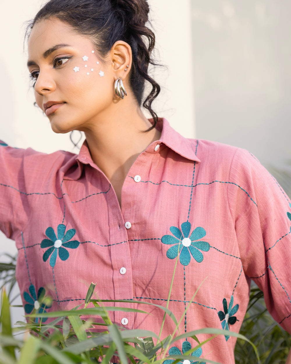 Woman wearing a pink checkered shirt with floral designs outdoors