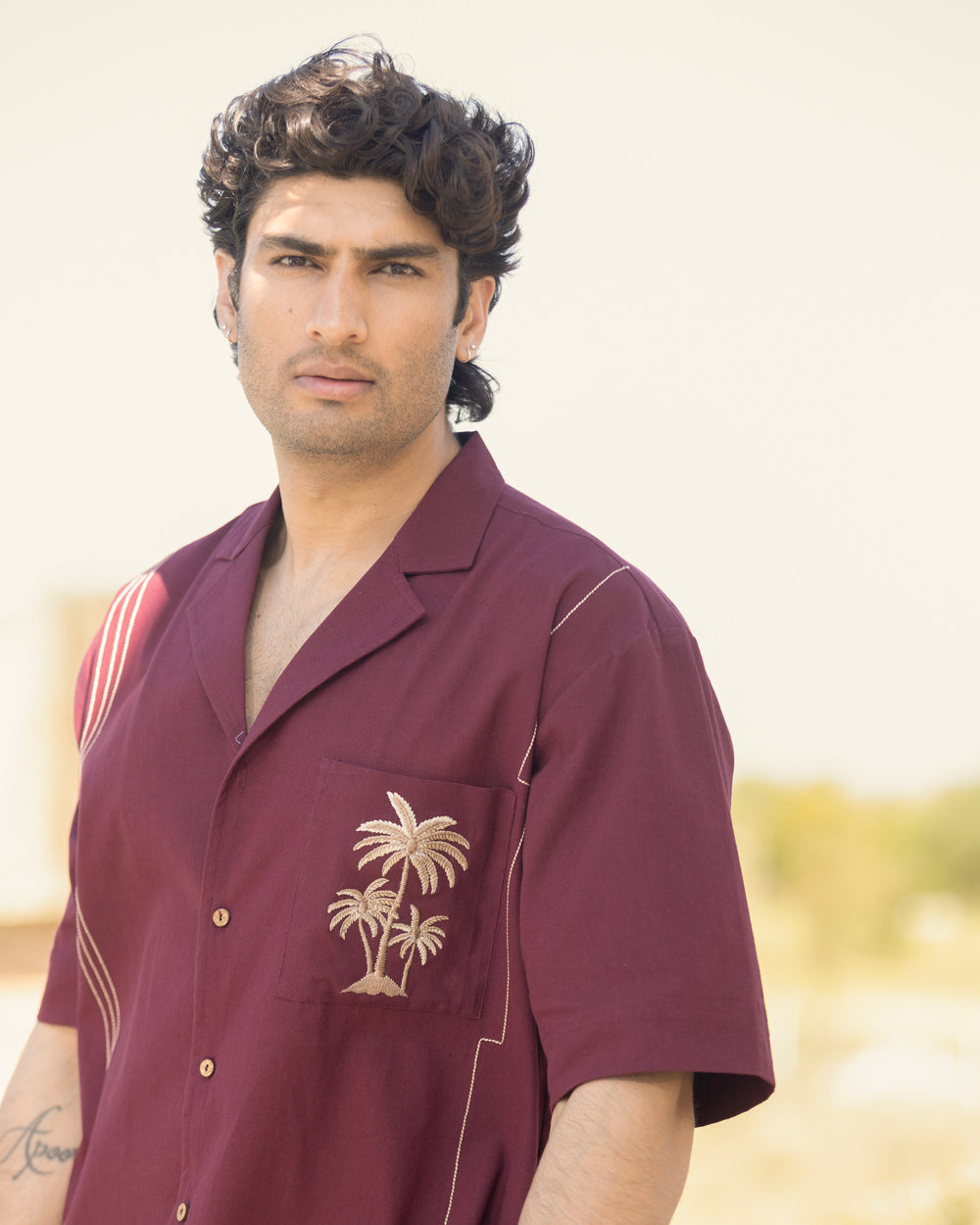 Man wearing a maroon shirt with palm tree design against a blurred background
