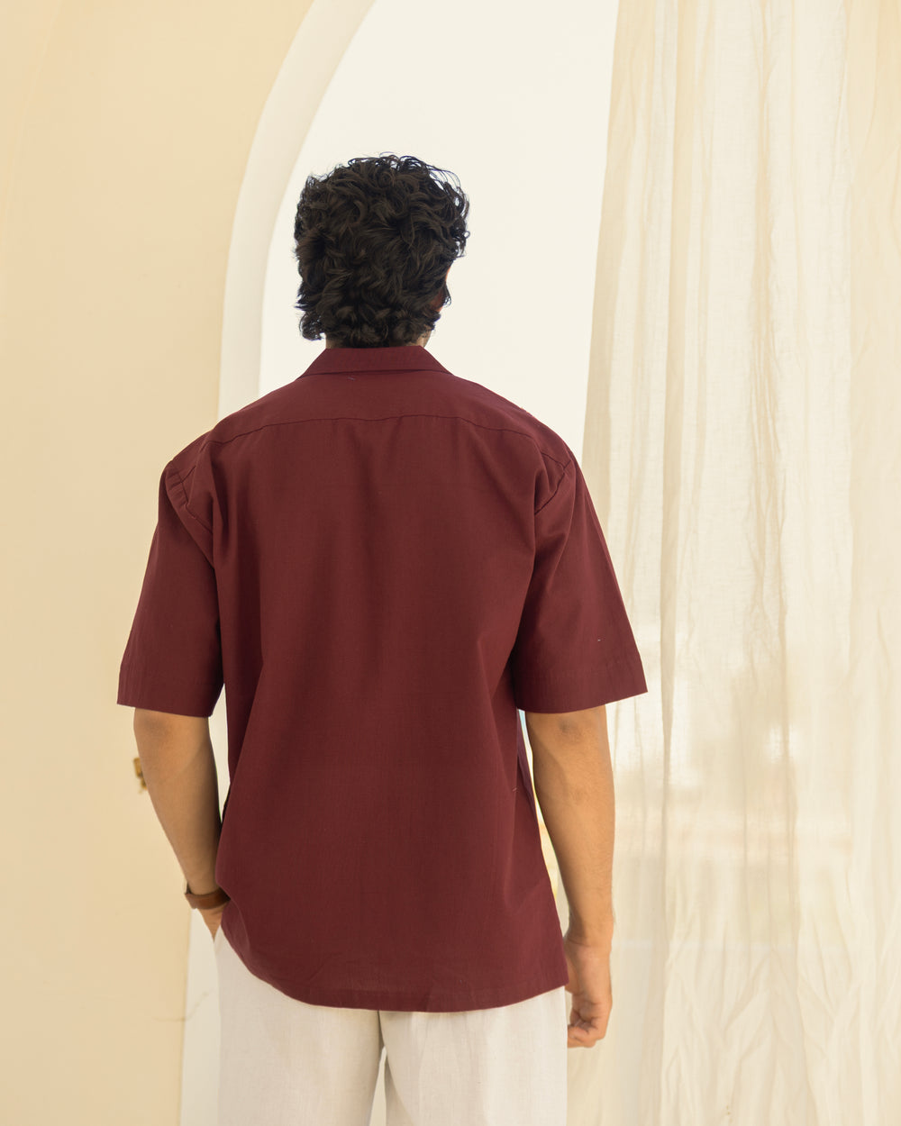 Person wearing a maroon shirt standing in front of a white curtain.
