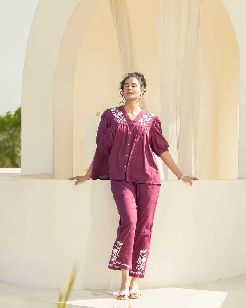 Woman in a maroon embroidered outfit standing against a white architectural background