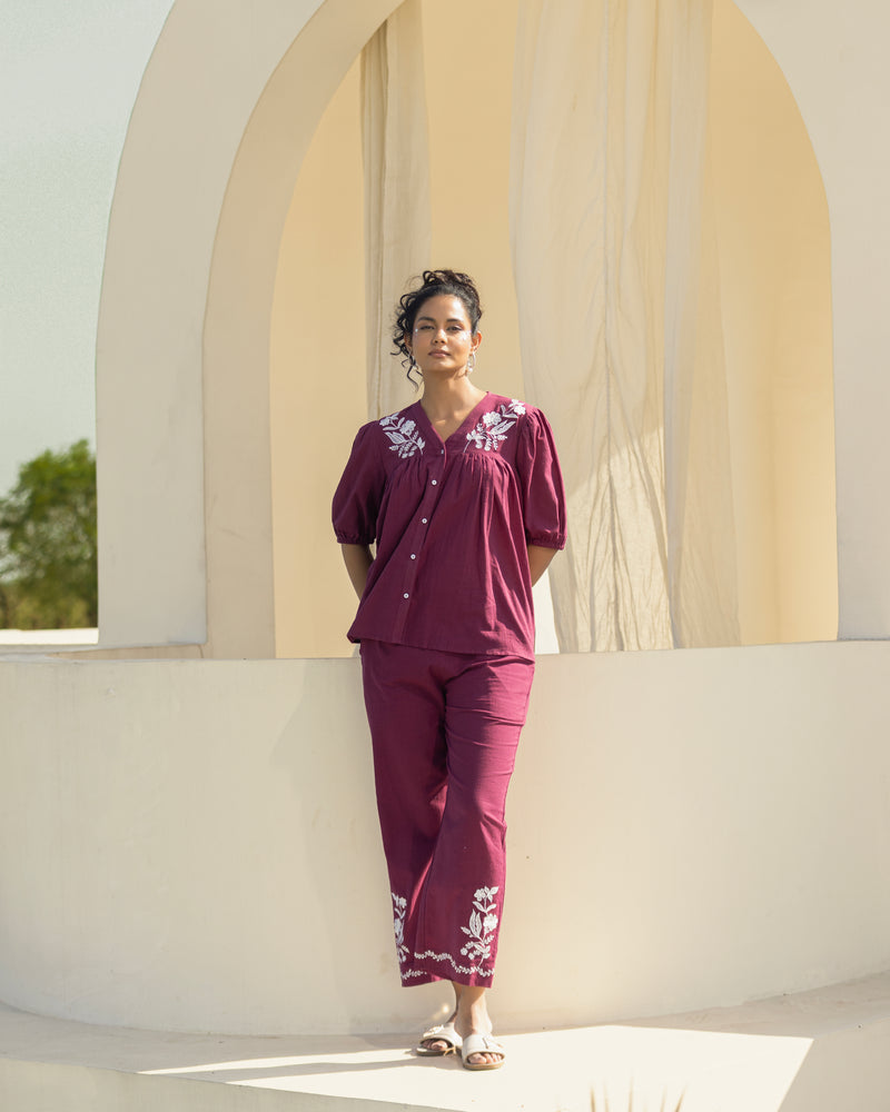 Woman wearing a maroon outfit with white patterns standing in front of a beige archway.