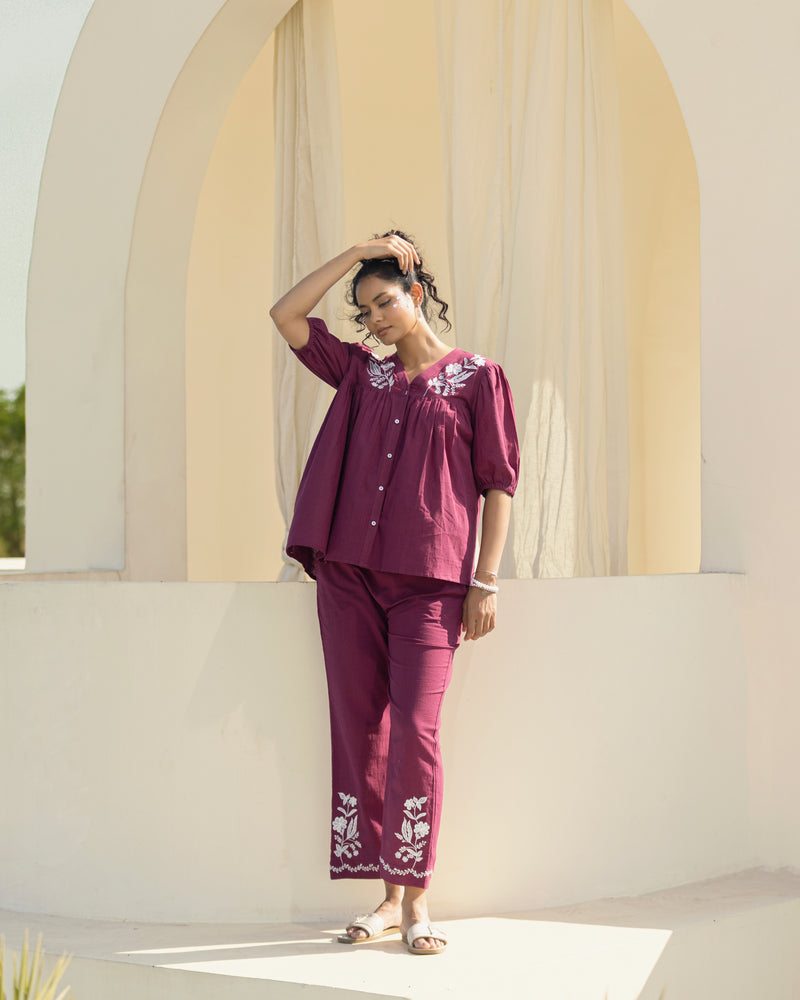 Woman in a purple outfit standing in front of a white archway with beige curtains.