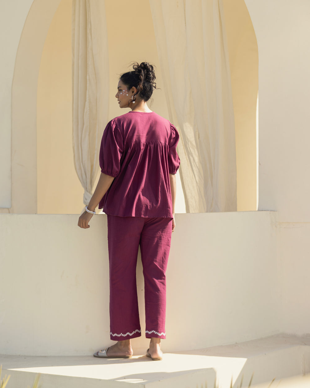 Woman in a burgundy outfit standing in front of a large window with light filtering through.