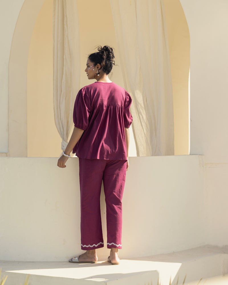 Woman in a burgundy outfit standing in front of a large window with light filtering through.