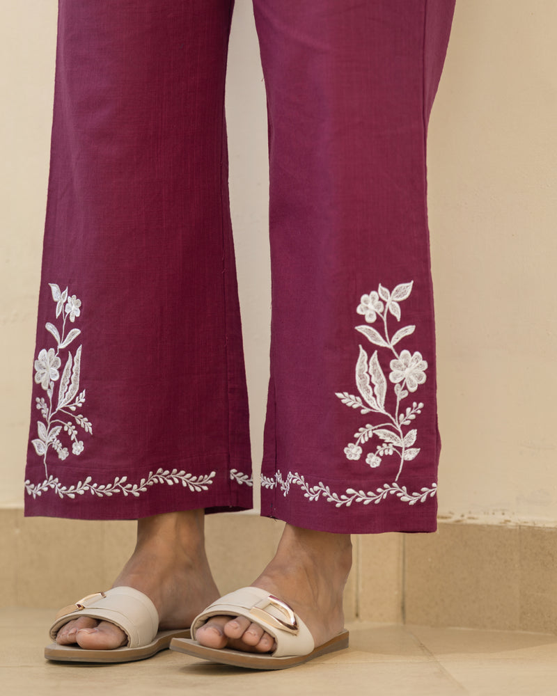 Maroon pants with white floral embroidery worn by a person on a beige background