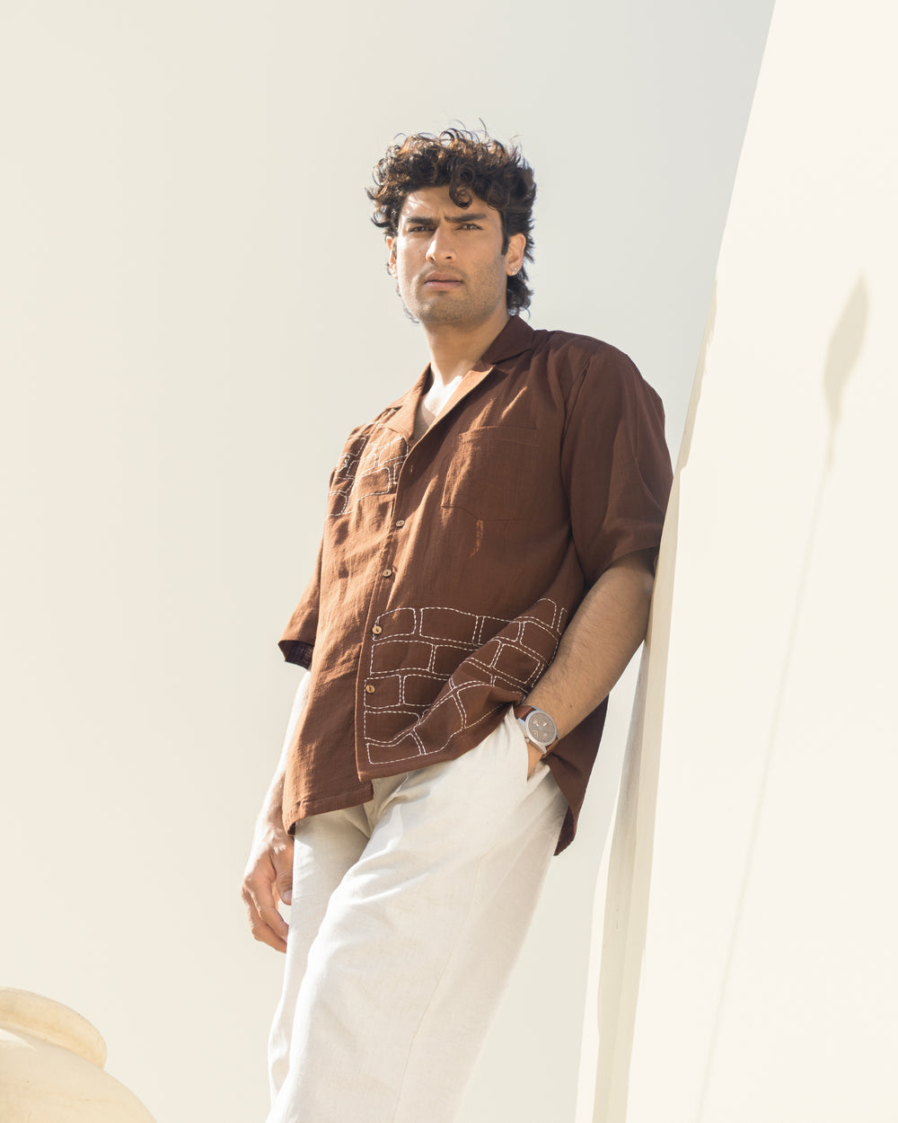 Man wearing a brown shirt and white pants against a light background